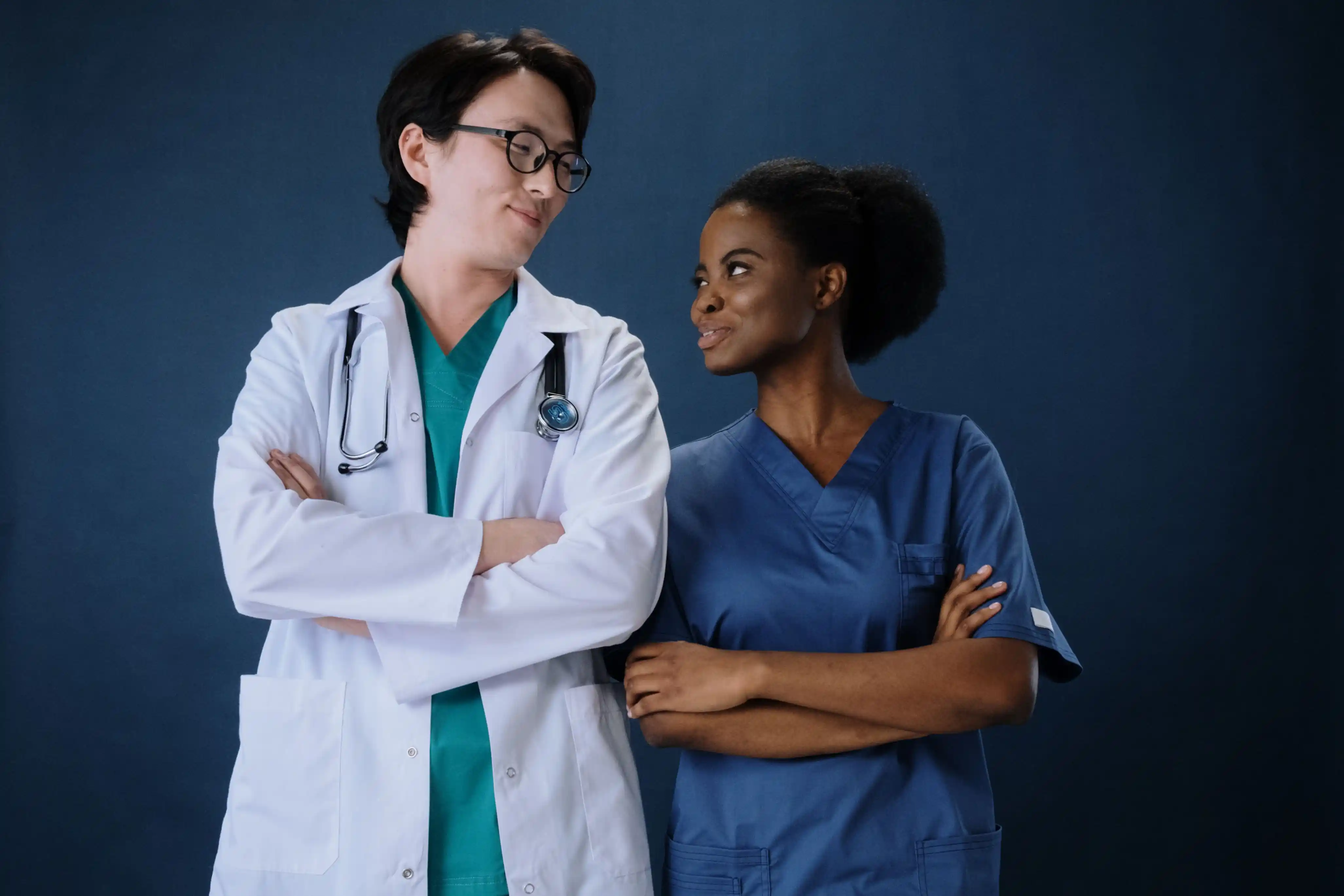 Two clinicians in scrubs and a white coat standing with arms folded