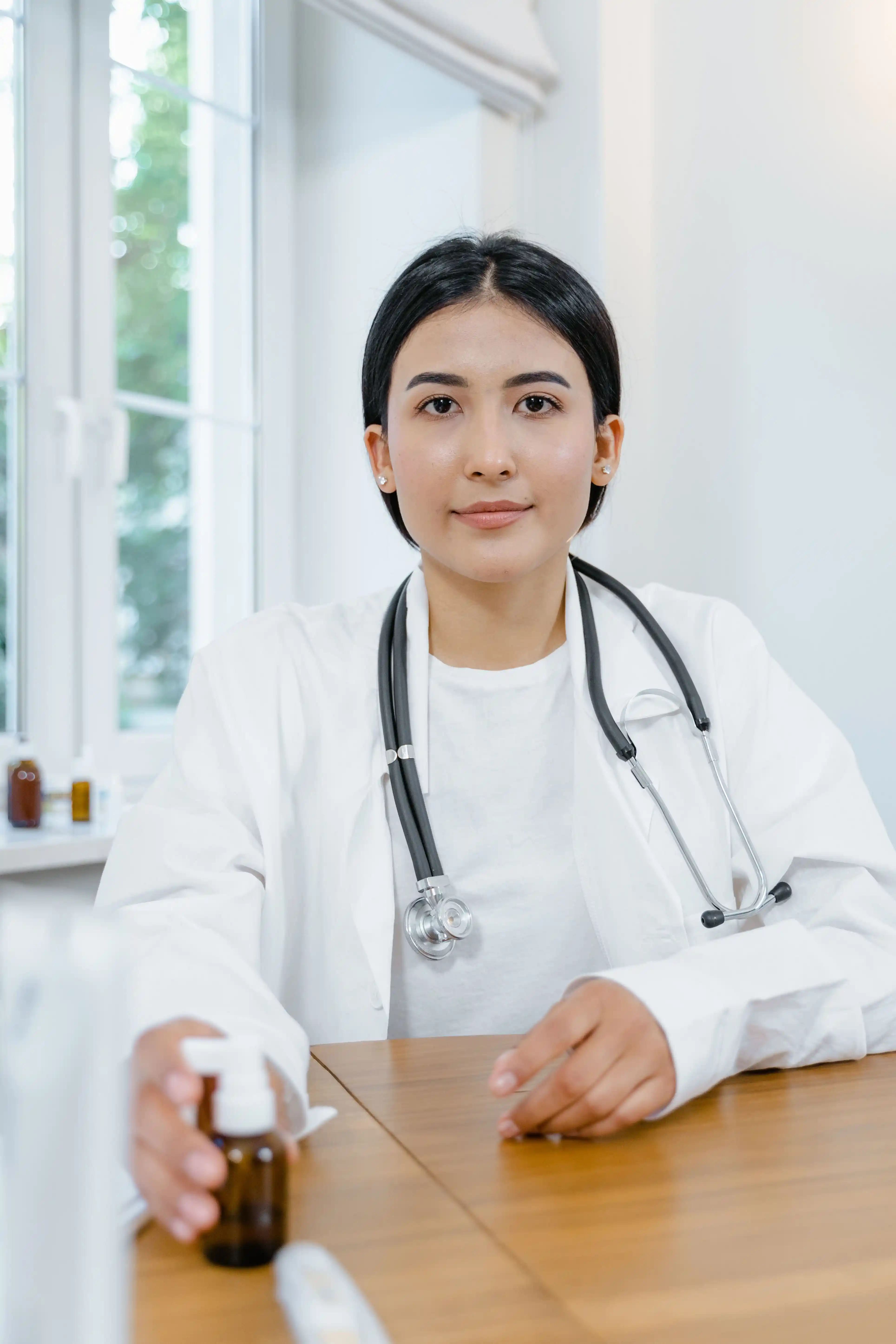 Smiling doctor in a white coat with a stethoscope, seated at a desk